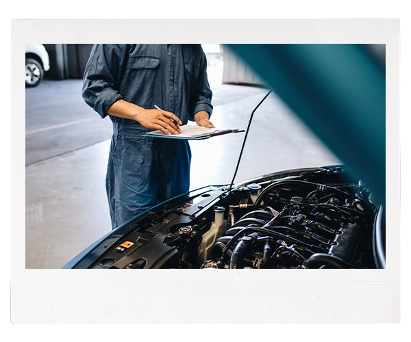 Technician with clipboard inspecting vehicle's engine bay