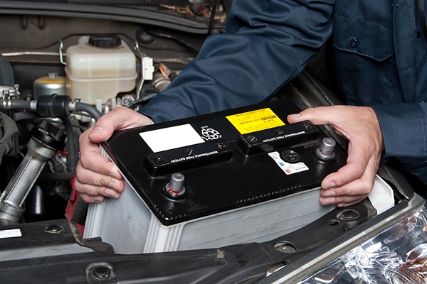 Technician installing new battery in engine bay